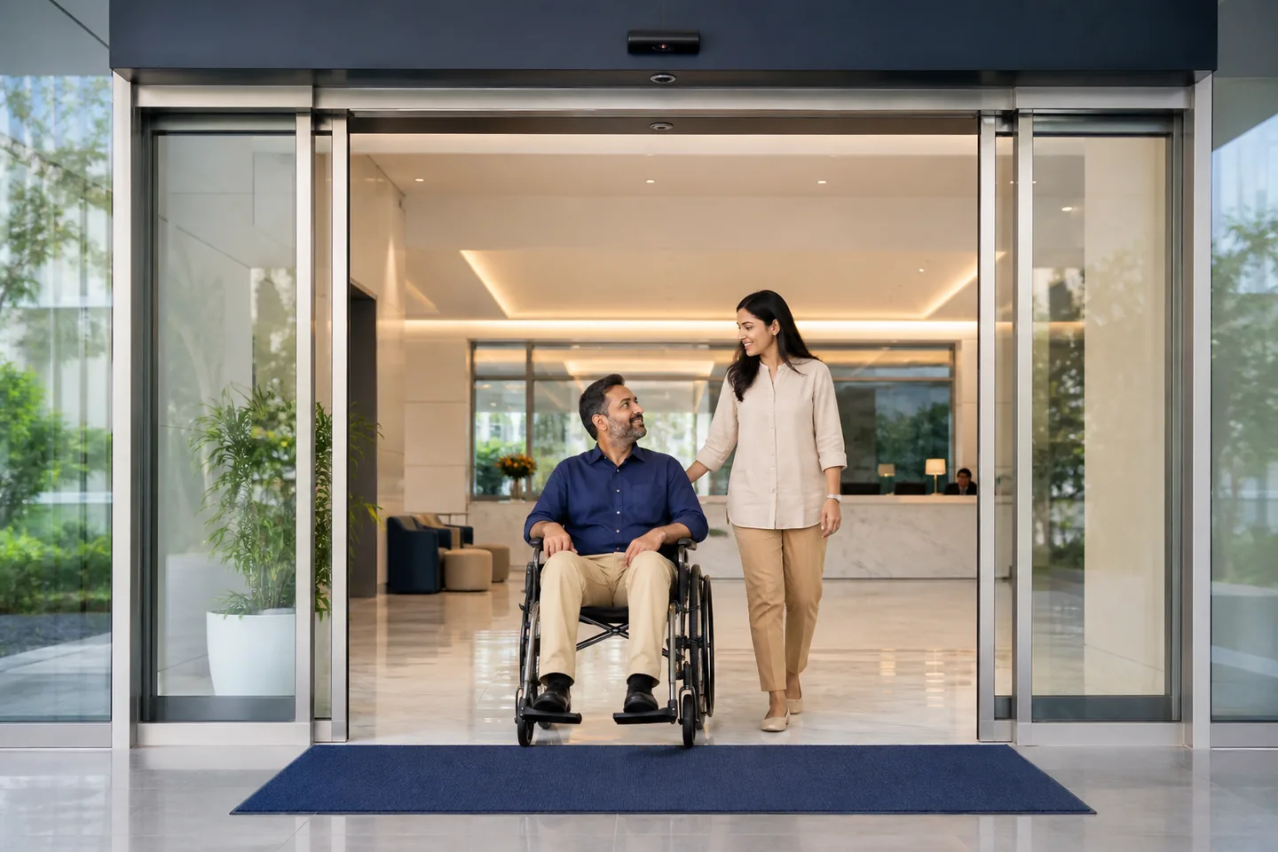 Wheelchair user and companion passing through an accessible automatic glass entrance